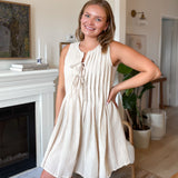 Woman in a beige dress standing in a living room with a fireplace and decor.